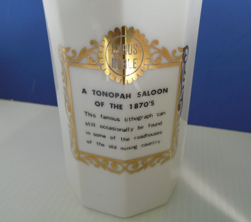 Description on white milk glass bottle from Cyrus Noble. Features the Tonopah Saloon of the 1870s. Photo with description of gambling scene.