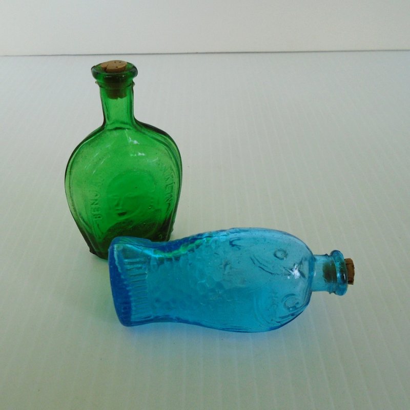 Two miniature bottles from the 1970s. One a fish and marked Fisch's Bitters, and one with the silhouette of Benjamin Franklin. 3 inches tall. 