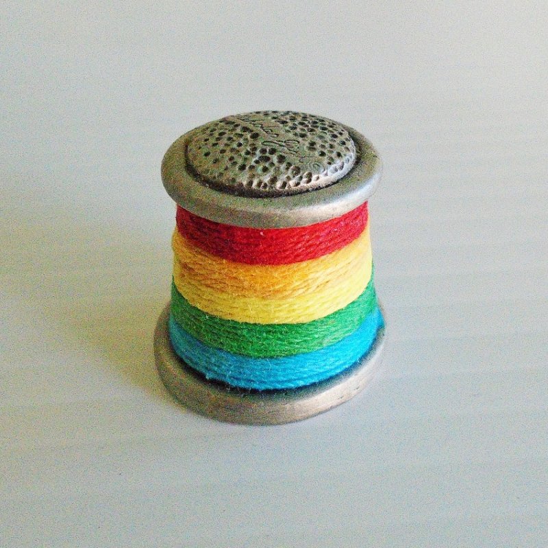Collectible souvenir pewter thimble of a multi color spool of thread. Signed Nicholas Gish. 1 inch tall. Unknown age, estate purchase.