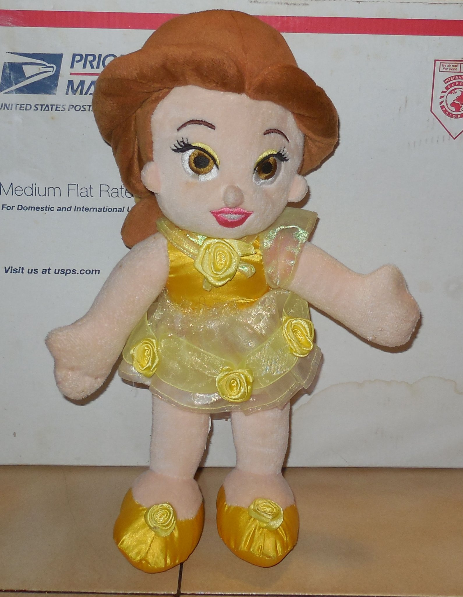 Front view of the authentic 12 inch Disney Belle plush doll wearing a yellow satin ball gown and holding a red rose.
