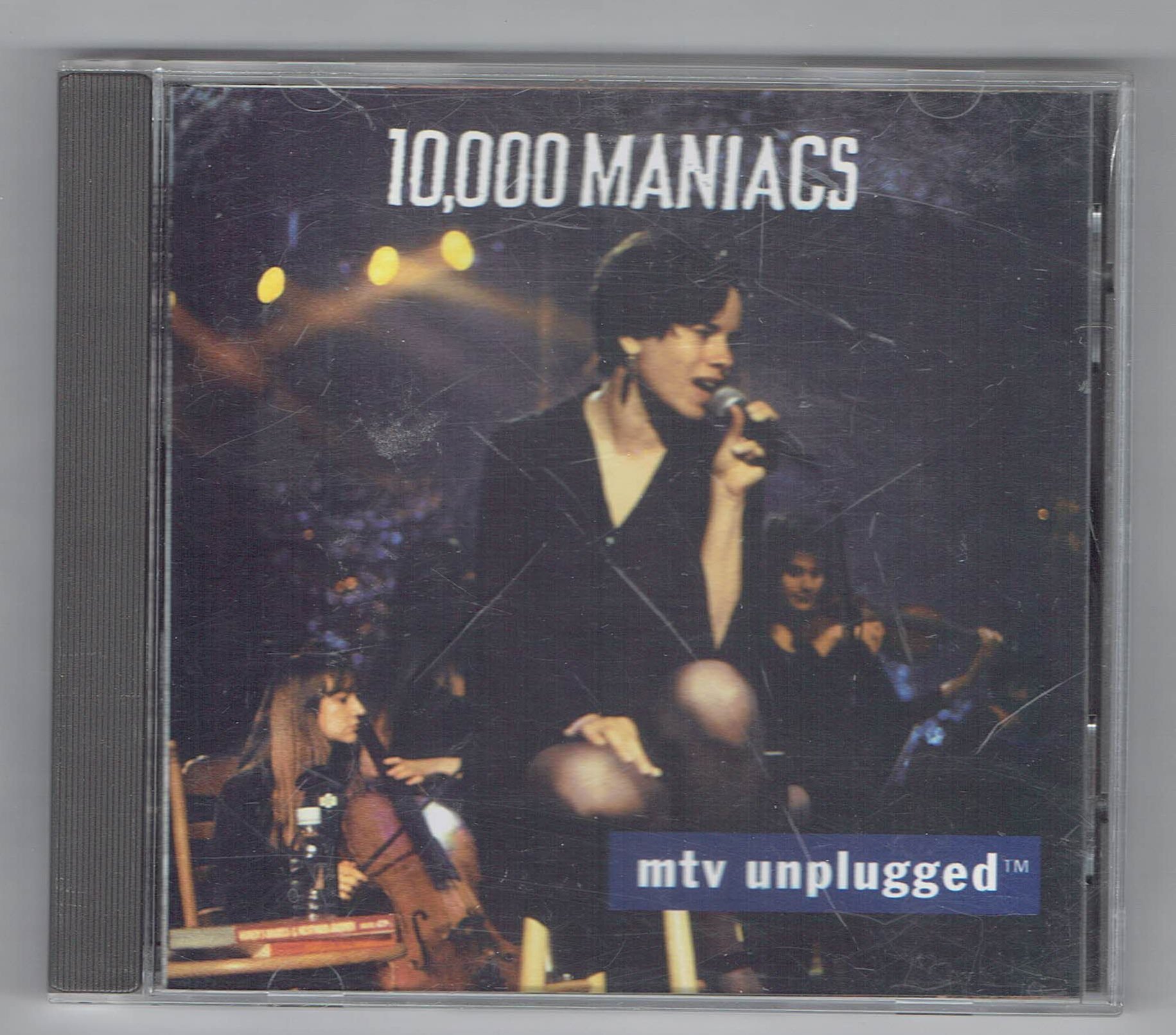 Front cover artwork of the 10,000 Maniacs MTV Unplugged CD showing Natalie Merchant singing live into a microphone with cello players in the background.